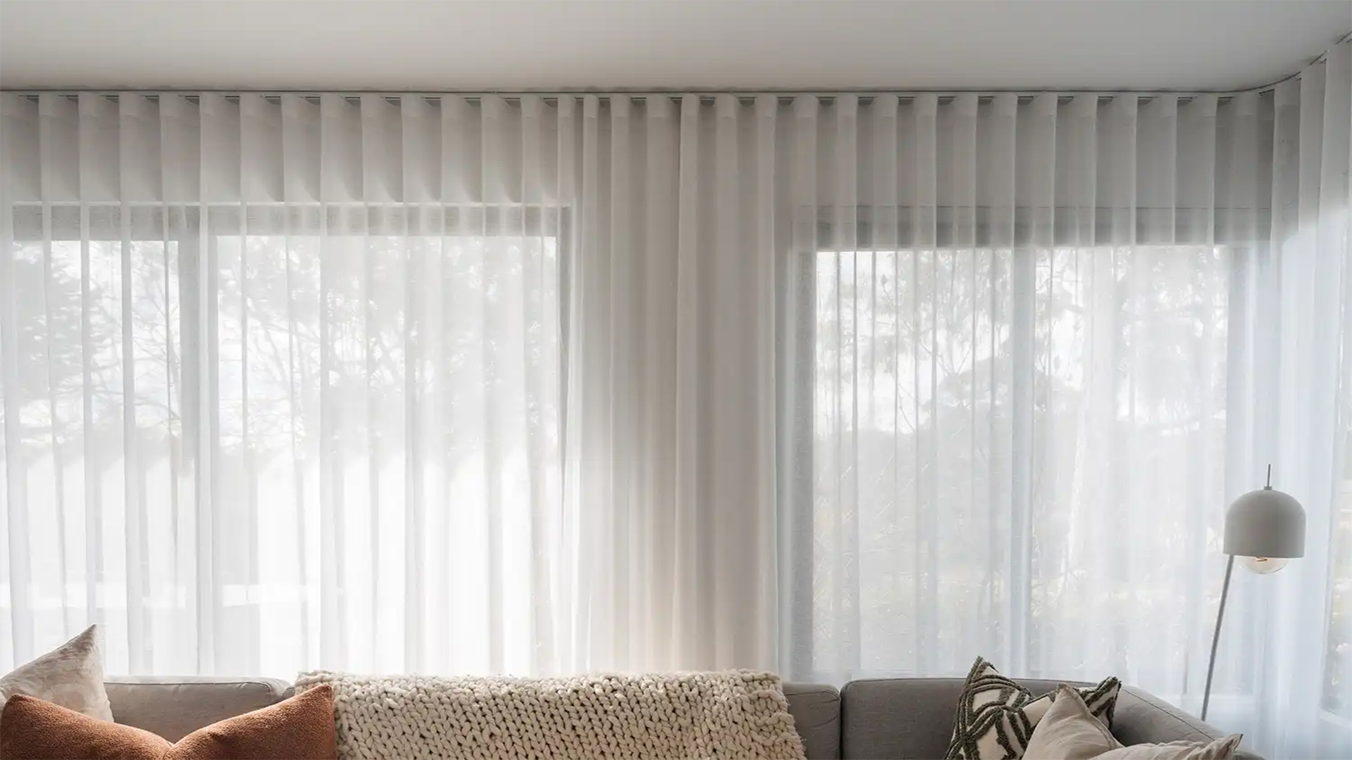 Cortinas de rieles con sistema de ondas perfectas y visillo blanco en el ventanal de una sala
